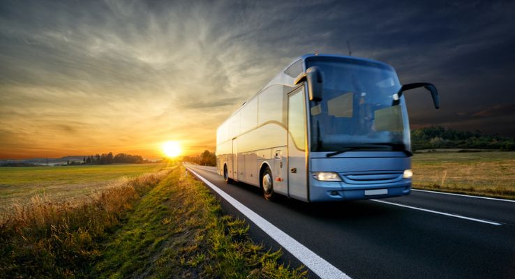 charter bus rental driving on an empty road at sunset